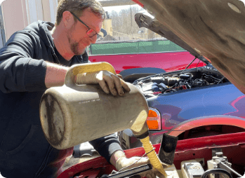 mechanic at ABS unlimited auto repair in Fairfax VA pouring fresh oil into car engine from oil pitcher while completing an oil change