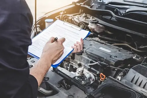 Multi-point Inspection | ABS Unlimited in Fairfax, VA. Closeup image of an auto mechanic spot checking a car engine with inspection checklist on a clipboard. Concept image of auto repair and maintenance.