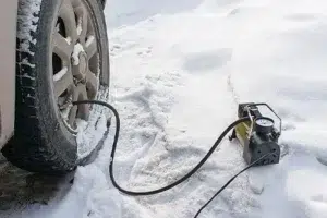 How to Winterize Your Car (and Save Money on Auto Repair) | ABS Unlimited in Fairfax, VA. Image of a tire and a pump beside it. The pump is used for inflating tires the flat tire of the car in winter.